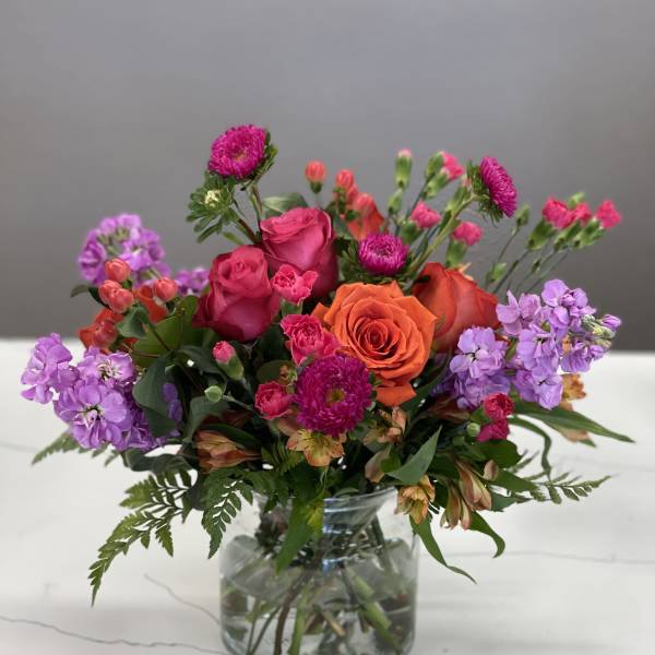 Mixed bouquet of pink, orange, and purple flowers in a clear glass vase
