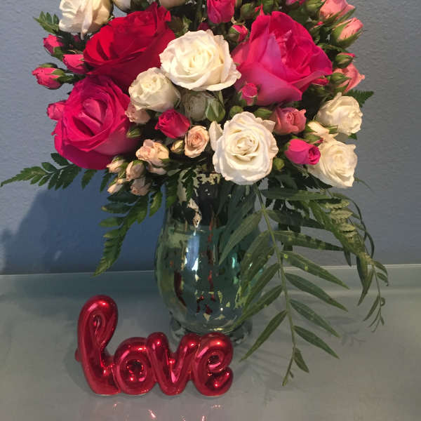 Bouquet of red, pink, and white roses in a glass vase with a red "love" decoration