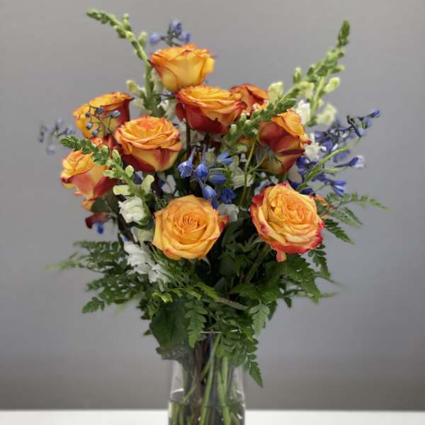 Orange roses with blue and white accent flowers in a glass vase
