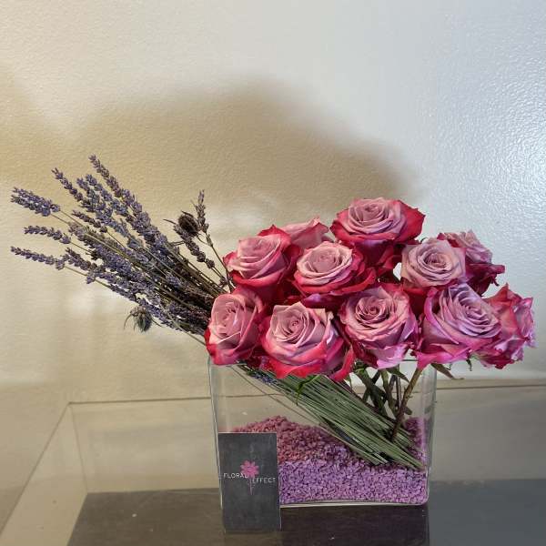 Pink roses arranged in a clear square vase with lavender sprigs