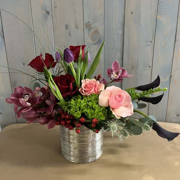 Mixed bouquet of roses, orchids, and tulips in a silver vase