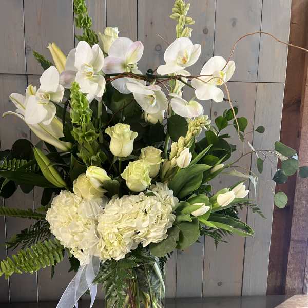 White orchids and pale flowers arranged in a clear glass vase with a ribbon.