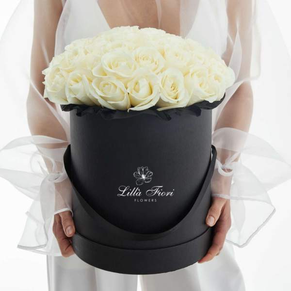 White roses arranged in a black round box with sheer ribbon