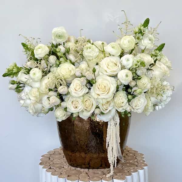 White rose bouquet in a brown vase with a ribbon tag