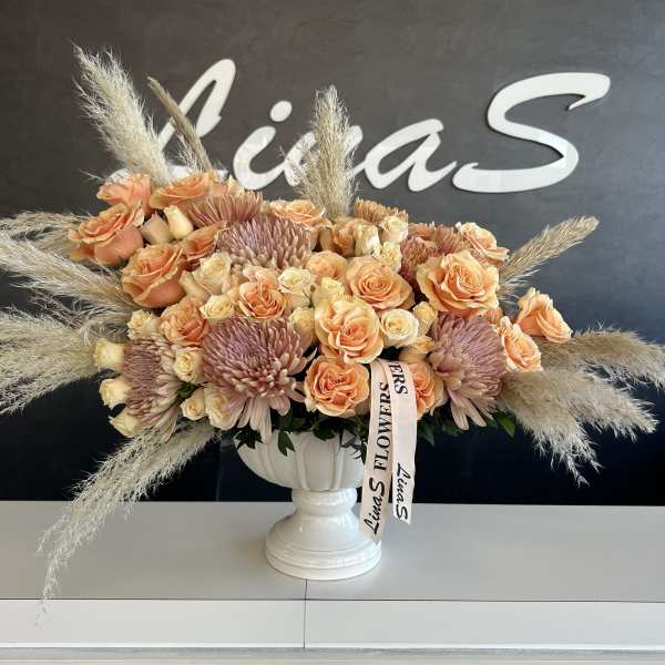 Peach roses and mauve chrysanthemums in a white pedestal vase