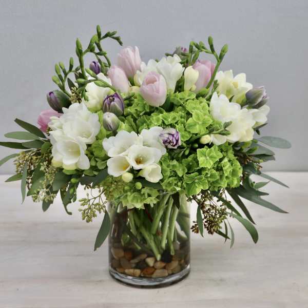 Pink and white flowers arranged in a glass vase with green blooms