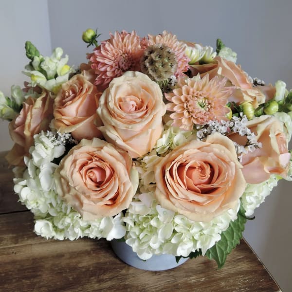Peach roses and white hydrangeas in a low round vase arrangement