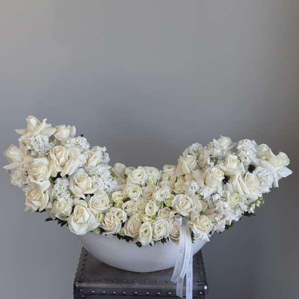 Large white rose arrangement in a white bowl vase