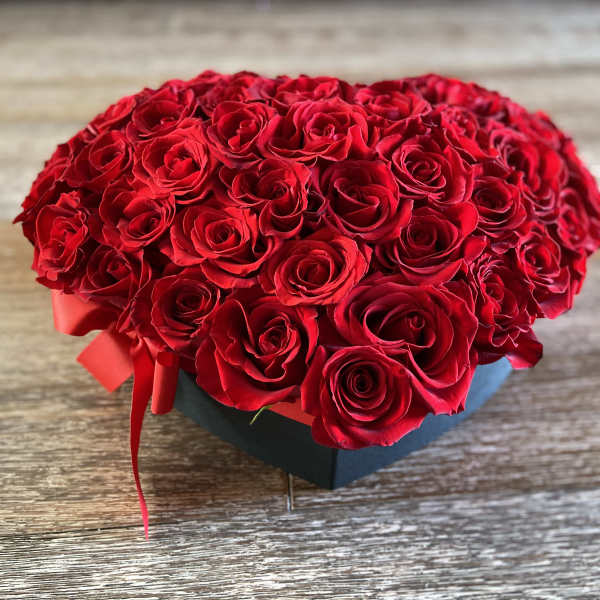 Heart-shaped box filled with red roses and a red ribbon