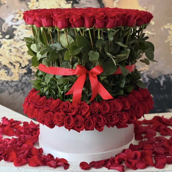 Tiered arrangement of red roses with a red ribbon on a white box