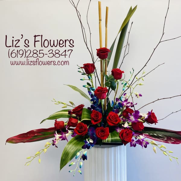 Tall arrangement of red roses and purple orchids in a white pedestal vase