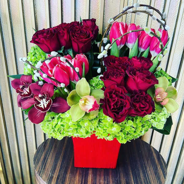 Bouquet of burgundy roses, pink tulips, and orchids in a red vase