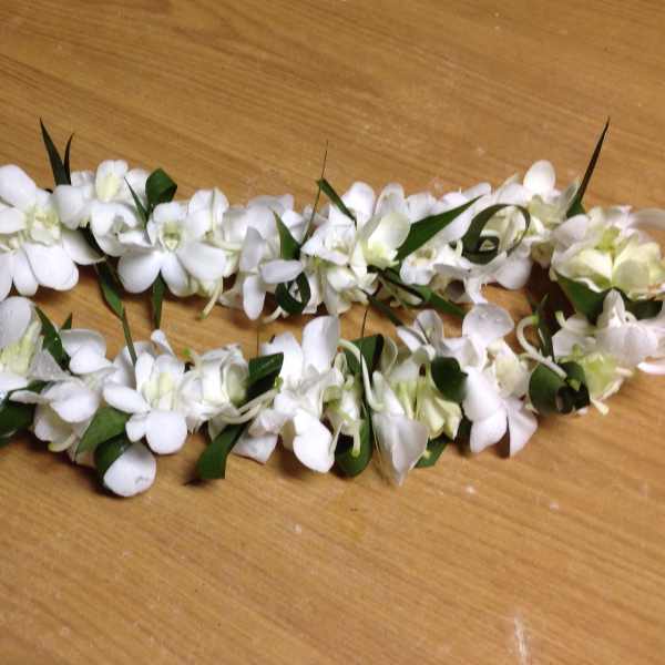 White floral lei with green leaves on a wooden surface