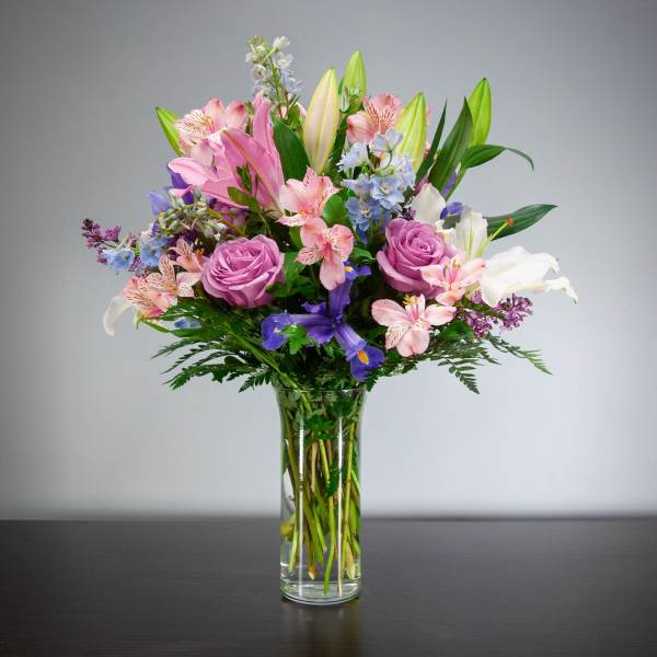 Mixed bouquet of pink, purple, and white flowers in a clear glass vase