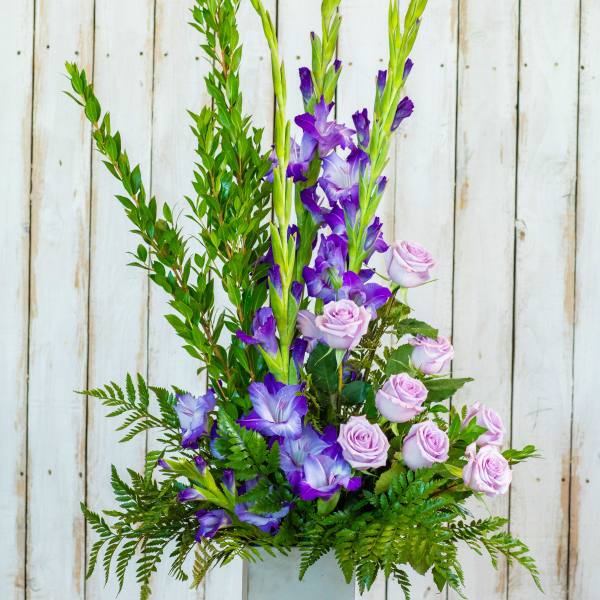 Tall floral arrangement with purple flowers and pale pink roses in a square vase