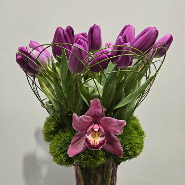 Purple tulips and an orchid in a glass vase with green moss
