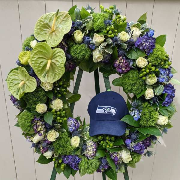 Large floral wreath with white roses, purple hydrangeas, and green anthuriums around a blue cap