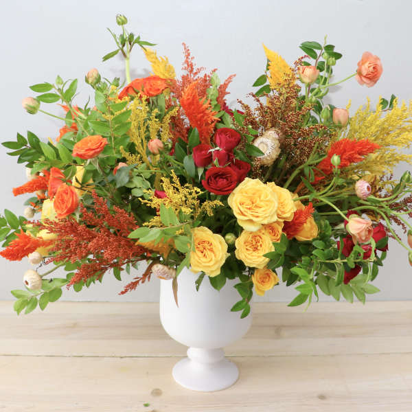 Colorful bouquet of roses and mixed blooms in a white pedestal vase