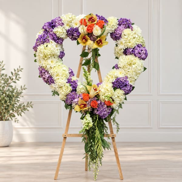 Heart-shaped floral wreath on a wooden easel with purple, white, and orange flowers