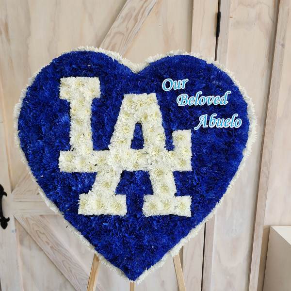 Heart-shaped floral tribute with blue and white flowers reading "LA" and "Our Beloved Abuelo"