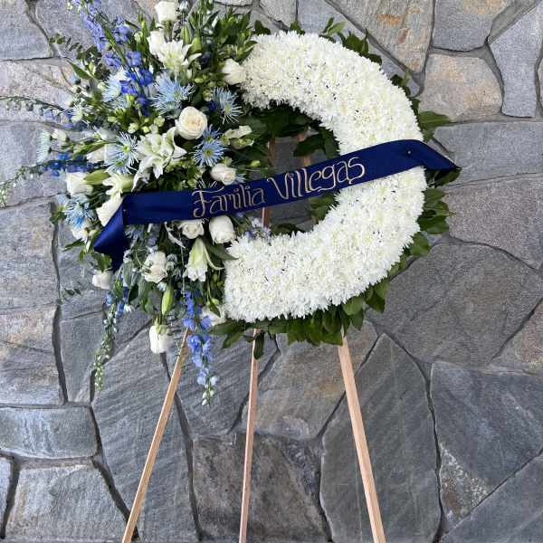 White floral wreath on an easel with blue and white flowers and a ribbon