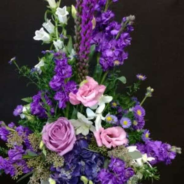Tall purple and pink floral arrangement in a white pedestal vase