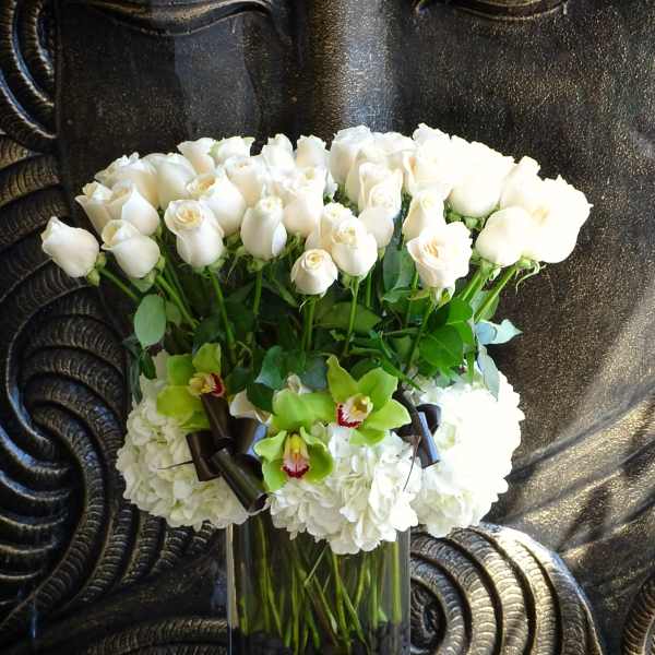 White roses and green orchids in a tall glass vase