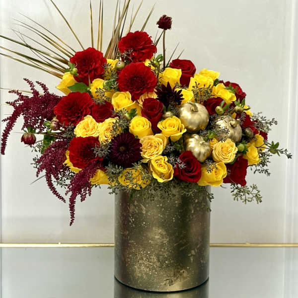 Red and yellow rose arrangement in a gold vase with gold pumpkins