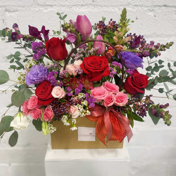 Mixed bouquet of roses, tulips, and purple blooms in a gift box with a ribbon