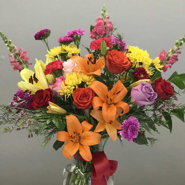 Mixed bouquet of lilies, roses, and chrysanthemums in a glass vase with a red ribbon