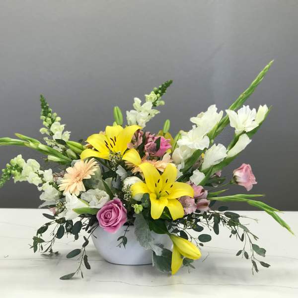 Mixed bouquet with yellow lilies, pink roses, and white snapdragons in a white bowl vase