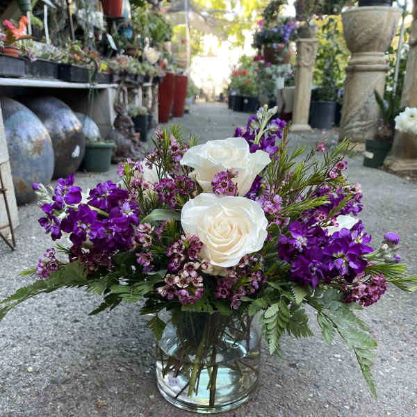 White roses and purple flowers arranged in a glass vase