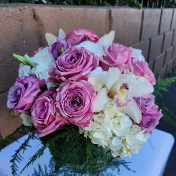 Round arrangement of pink roses, white hydrangeas, and orchids on a white pedestal