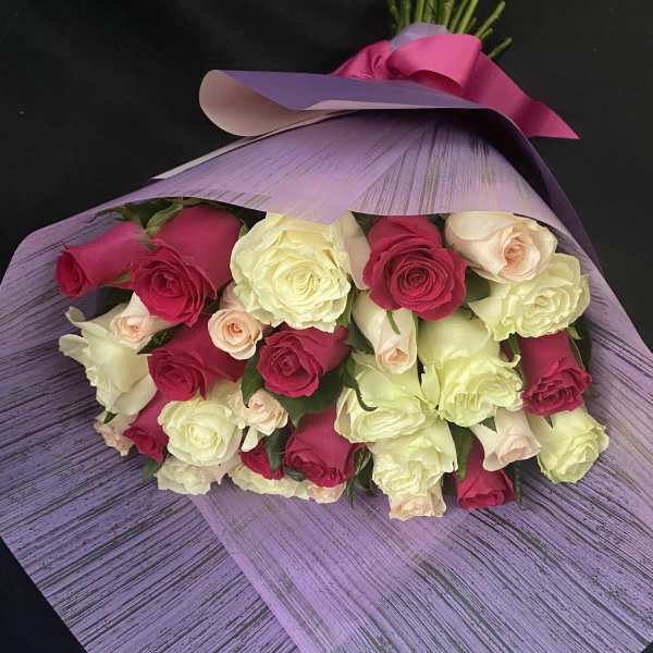 Bouquet of pink, cream, and pale yellow roses wrapped in lavender paper