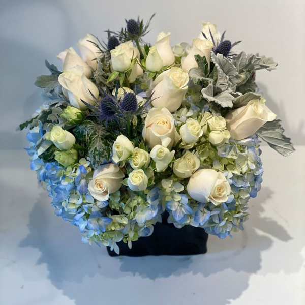 Bouquet of white roses, blue hydrangeas, and thistle in a black container