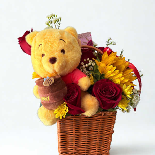Wicker basket with a teddy bear and red roses, sunflowers, and small white flowers
