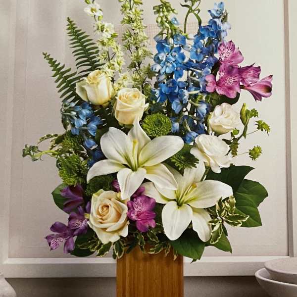 Tall floral arrangement with white lilies, cream roses, blue delphinium, and purple alstroemeria