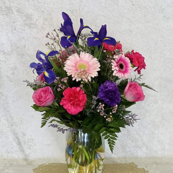 Mixed bouquet of pink, purple, and blue flowers in a clear glass vase