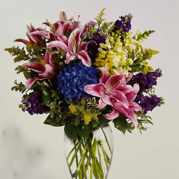 Bouquet of pink lilies, blue hydrangea, and purple flowers in a clear glass vase