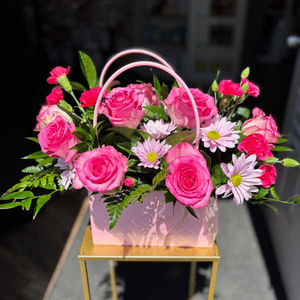 Pink roses and daisies arranged in a pink handled gift box