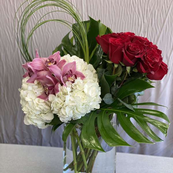 Bouquet of red roses, white hydrangeas, and pink orchids in a glass vase