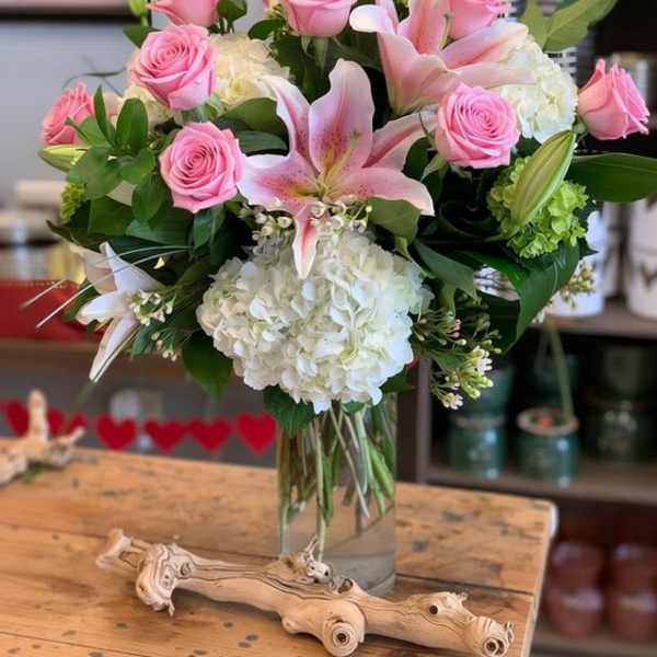 Vase arrangement of pink roses, white hydrangeas, and pink lilies in a clear glass cylinder