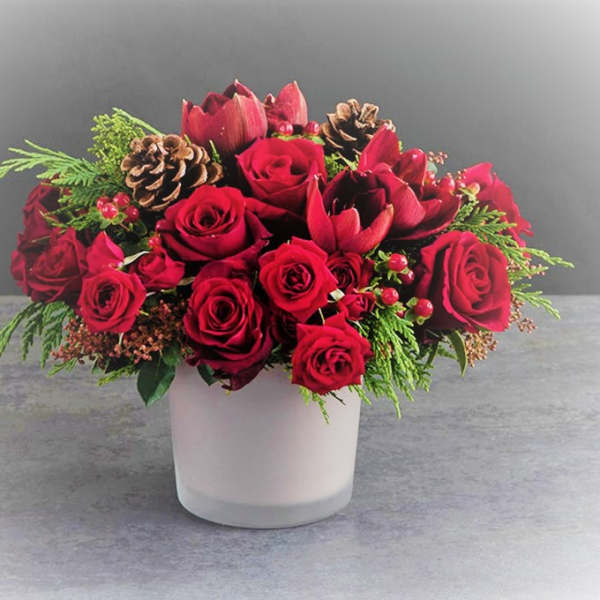 Red rose arrangement in a white vase with pinecones and greenery