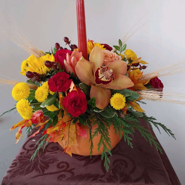 Autumn floral centerpiece with red candle in a pumpkin vase