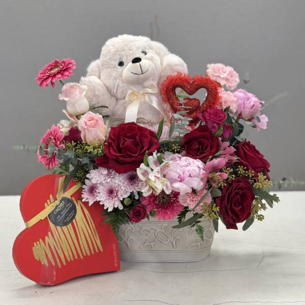 Teddy bear in a heart-shaped floral arrangement with red and pink flowers