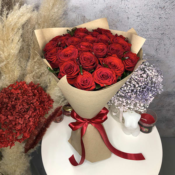 Large bouquet of red roses wrapped in brown paper with a red ribbon on a white table