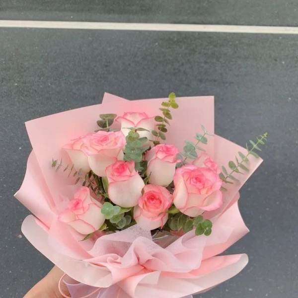 Handheld bouquet of pink roses wrapped in pale pink paper
