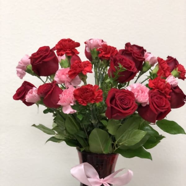Red roses and pink carnations in a burgundy vase with a pink ribbon