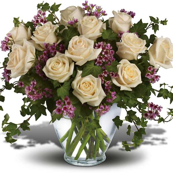 Cream roses and purple filler flowers in a clear glass vase