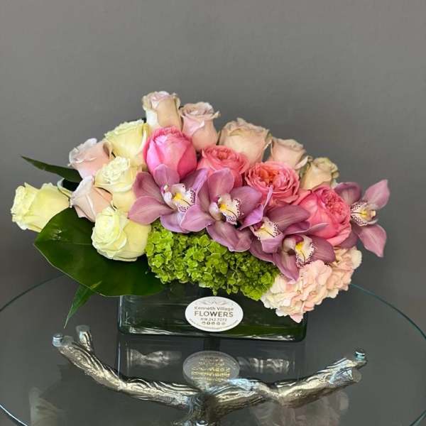 Pink and cream roses with purple orchids in a glass vase